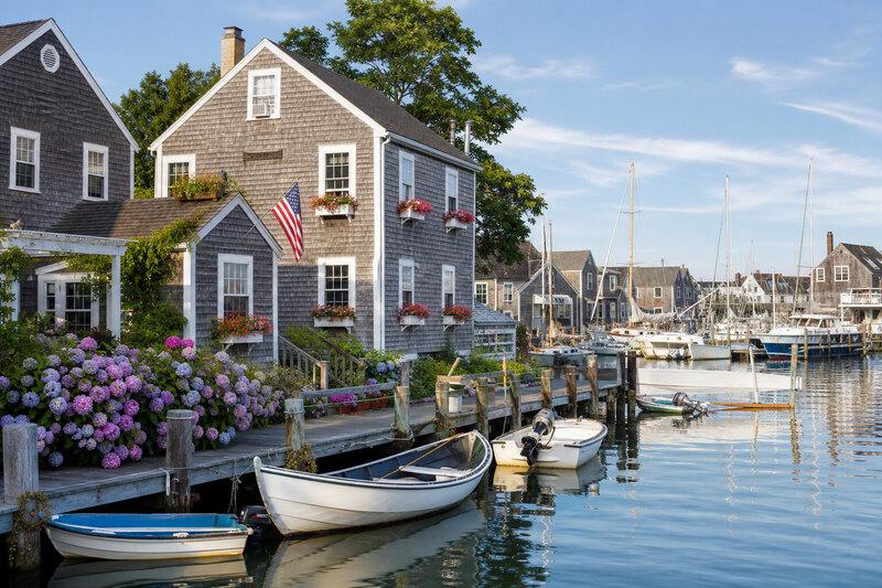 Gray shingled Cape Cod homes along a harbor dock with small boats