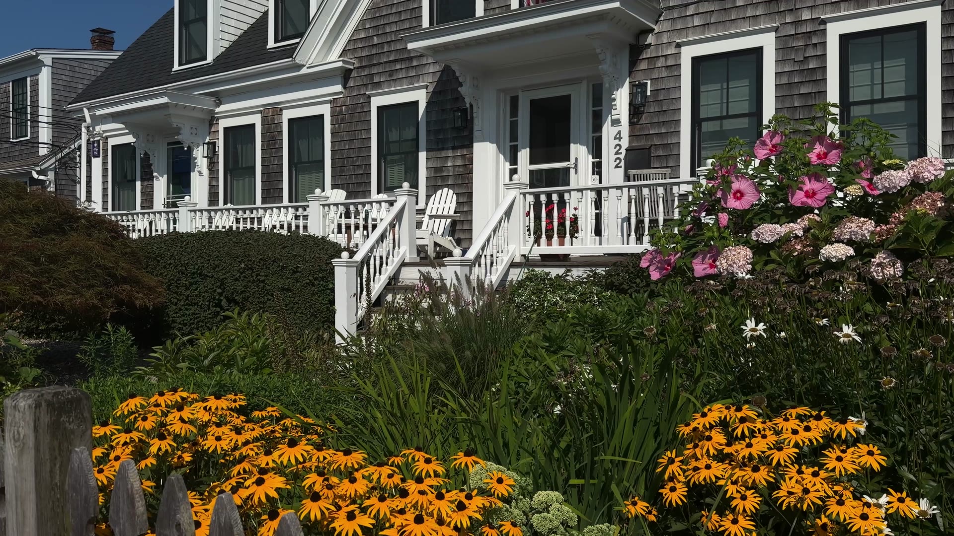 Exterior of a gray-shingled Cape Cod home with black-eyed Susans and a hibiscus garden to check during a final walk-through